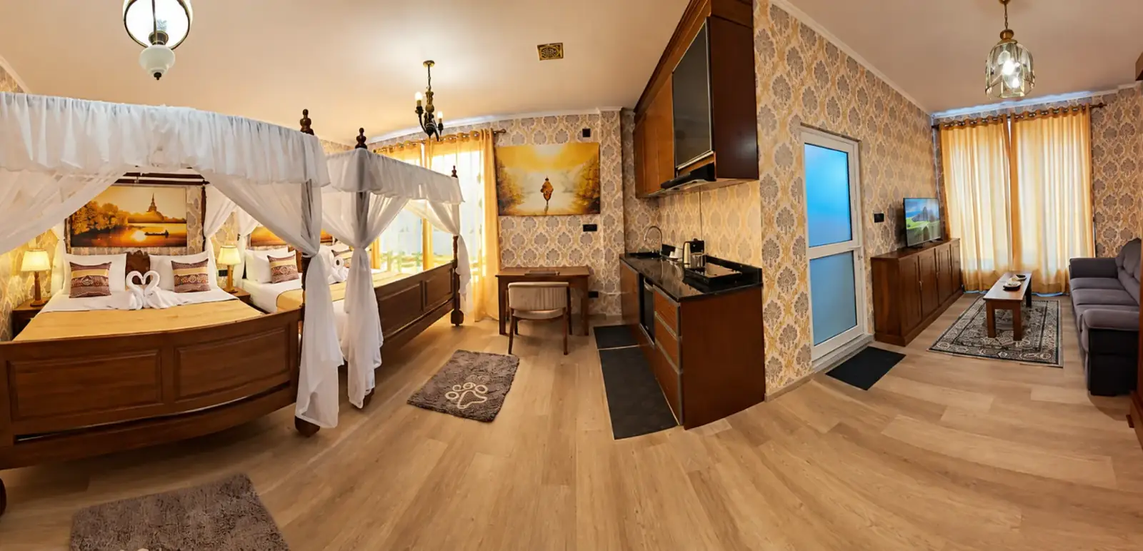 Wide panoramic view across a spacious room with two canopy beds, a kitchenette and a lounge area